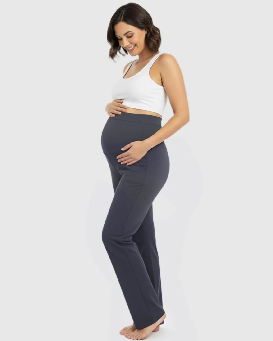 Smiling pregnant woman in dark gray stretch flared maternity pants with an over-belly waistband and pockets.