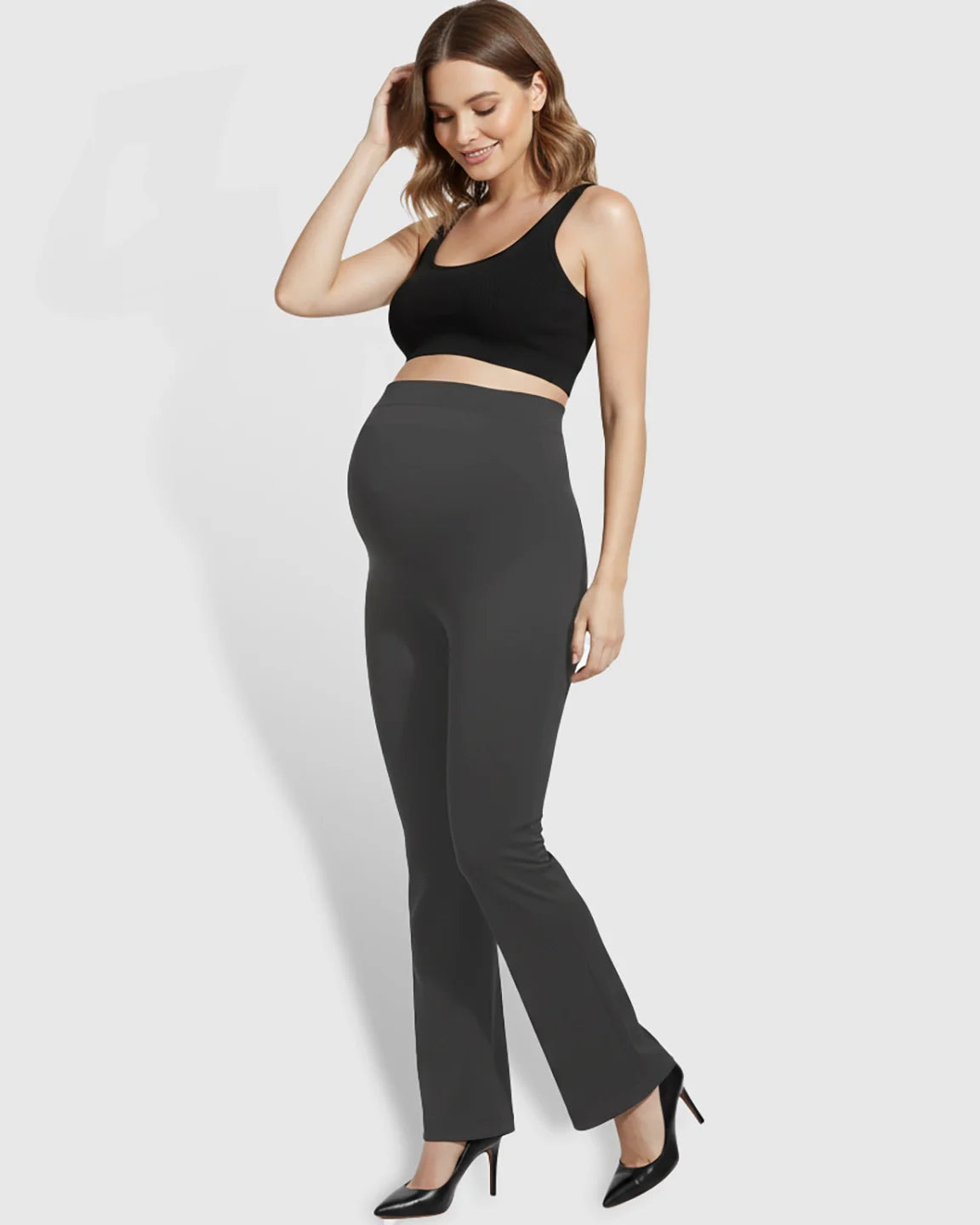 Smiling pregnant woman models charcoal gray over-belly bootcut maternity pants with a soft flare.