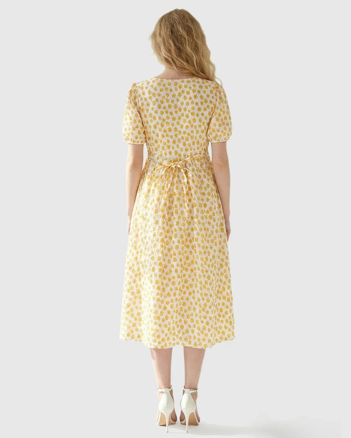 Woman from behind in a white and yellow floral print midi nursing dress with puff sleeves and a tie waist.