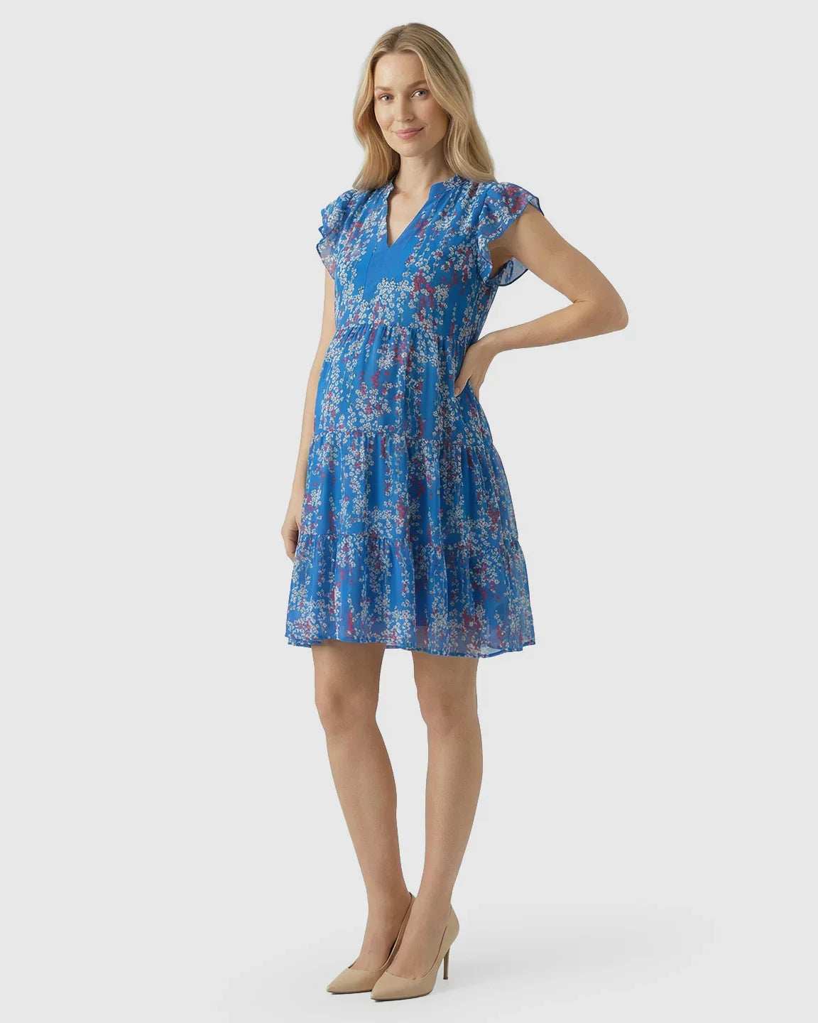 Blonde pregnant woman in a blue floral chiffon V-neck A-line maternity dress with flutter sleeves.