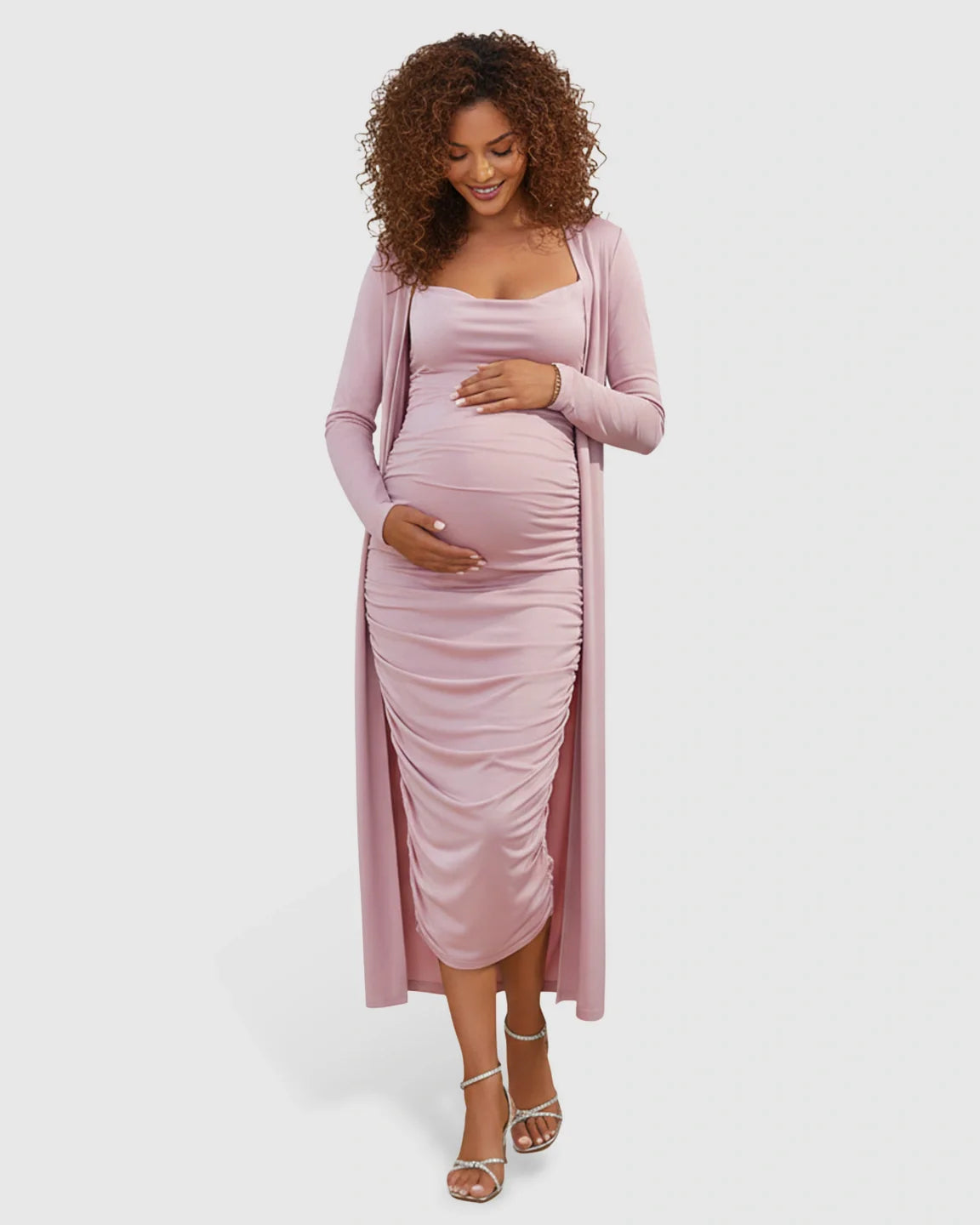 Pregnant woman in a pink side-ruched slip dress and long-sleeve cardigan maternity set.