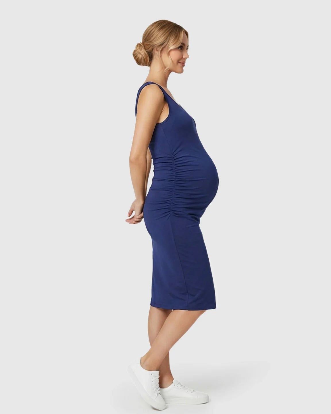 Navy sleeveless bodycon maternity dress with side ruching, worn by a smiling pregnant woman.