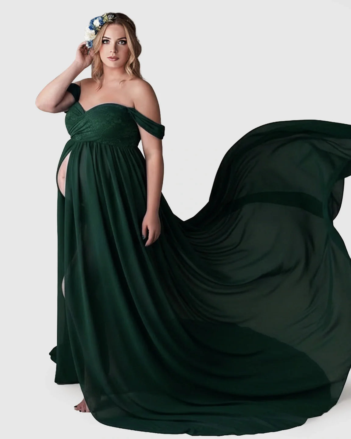 Pregnant woman in an off-shoulder, dark green chiffon maternity gown with a flowing train and front slit.