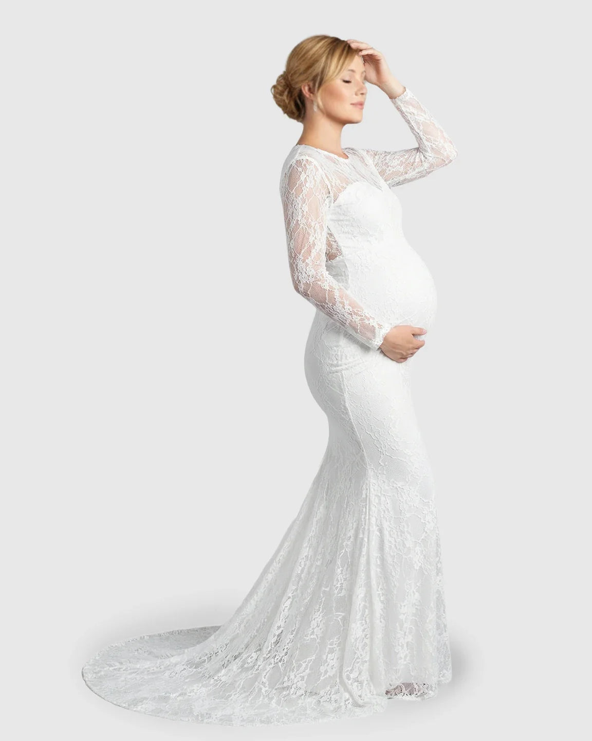 Pregnant woman in a white sheer lace trumpet maternity photoshoot gown with long sleeves and a mermaid skirt.