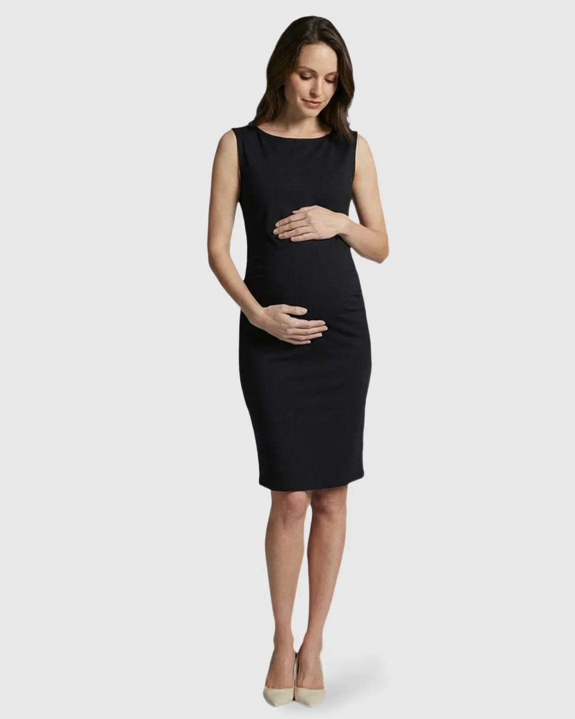 Pregnant woman in a black sleeveless bodycon maternity midi dress, gently holding her belly.