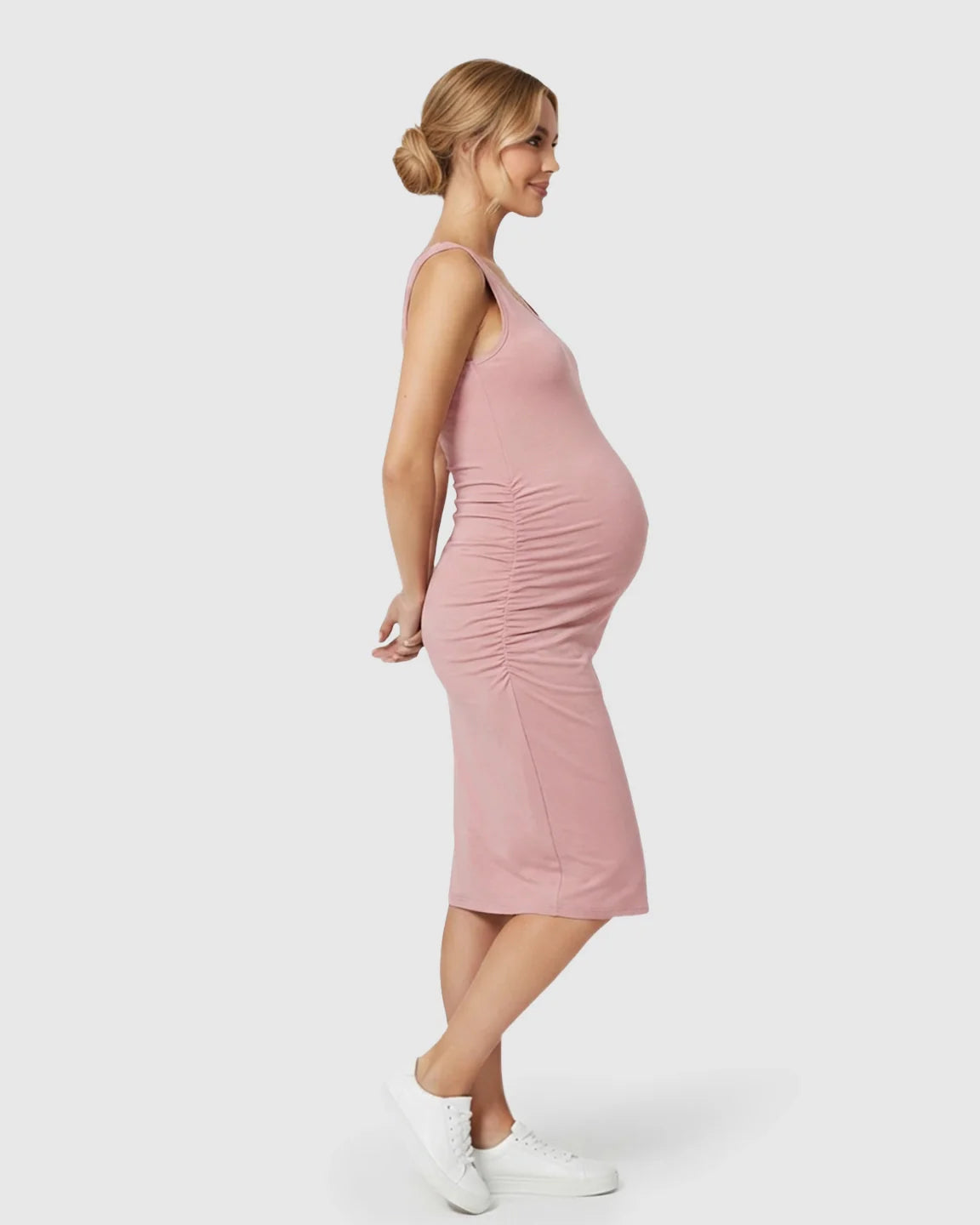Smiling pregnant woman in a pink sleeveless bodycon maternity dress with side ruching.