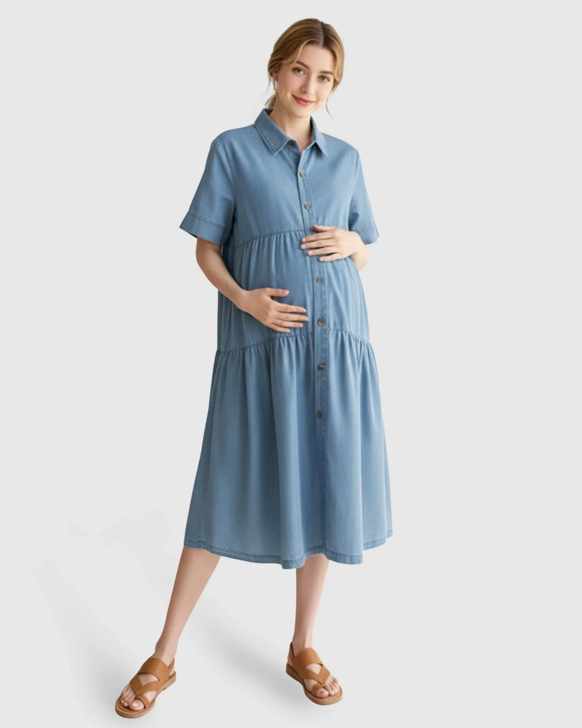 Pregnant woman in a blue tiered denim casual maternity midi dress with button-front and short sleeves.