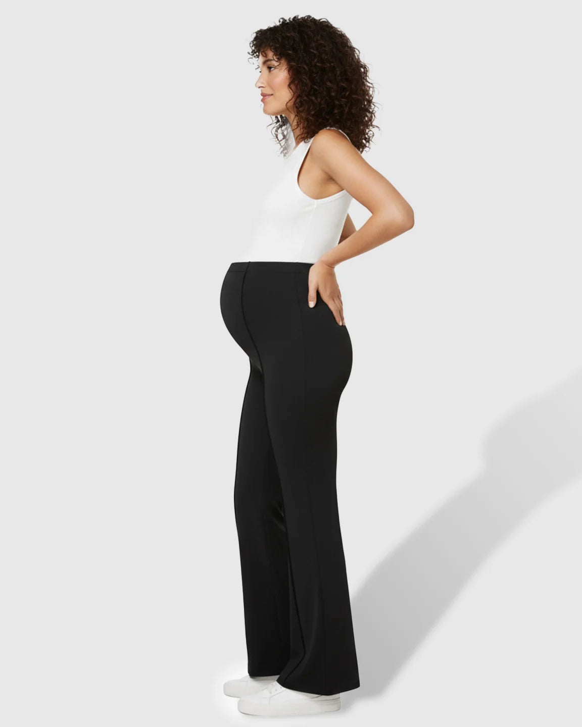 Pregnant woman in black butt-lifting flared maternity pants with an over-belly fit and white tank top.
