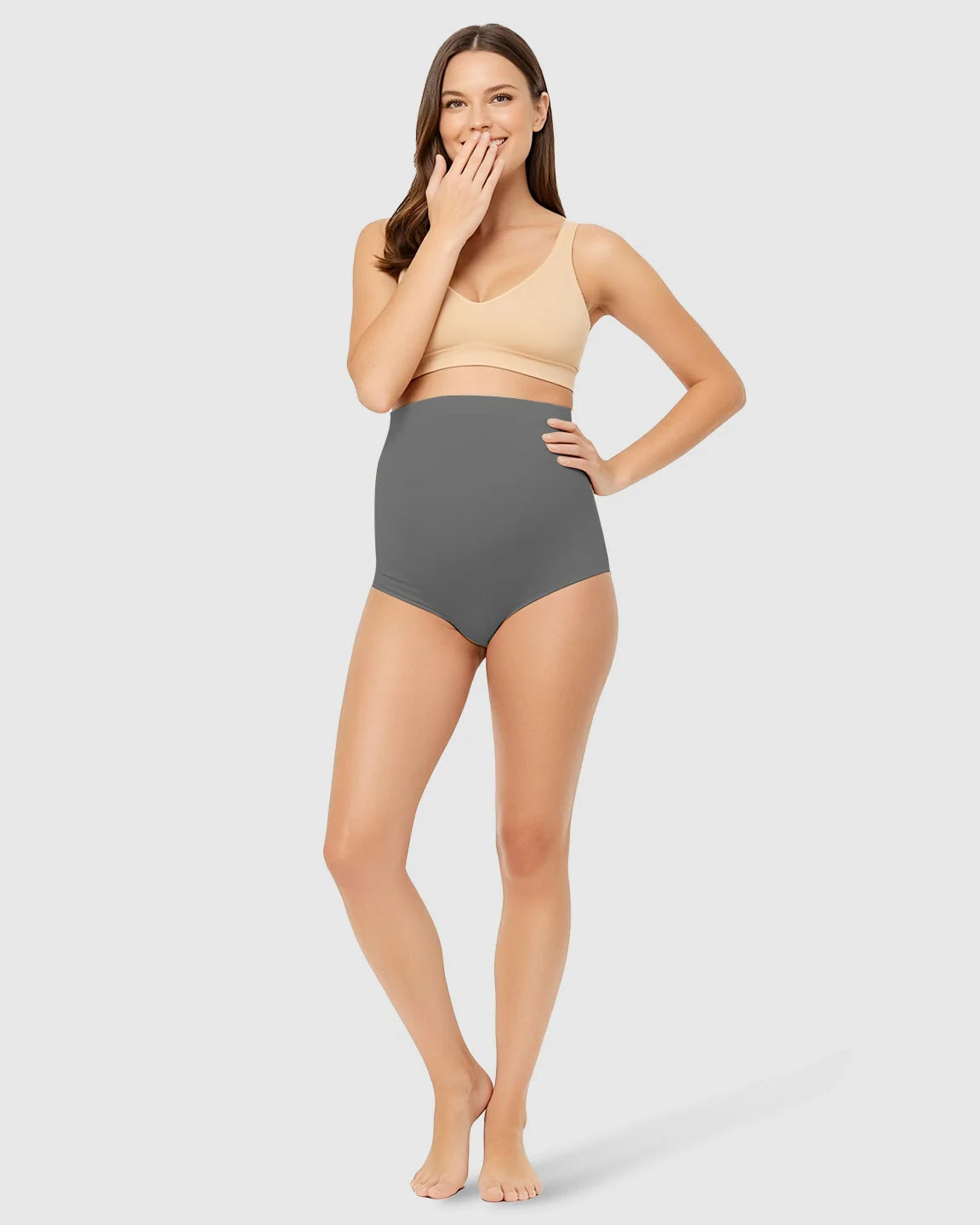 Smiling woman models grey high-waist seamless belly-support maternity underwear.