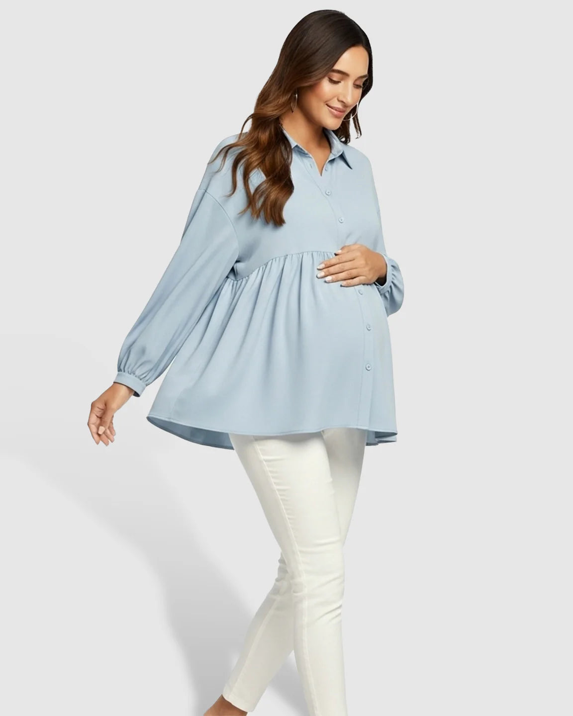 Maternity model in a light blue chiffon babydoll lapel long sleeve shirt and white pants, holding her bump.