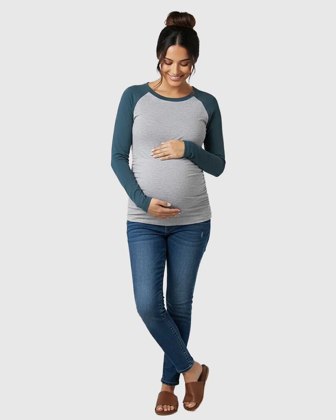 Smiling pregnant woman in a gray and teal raglan sleeve maternity top with ruched sides and blue jeans.