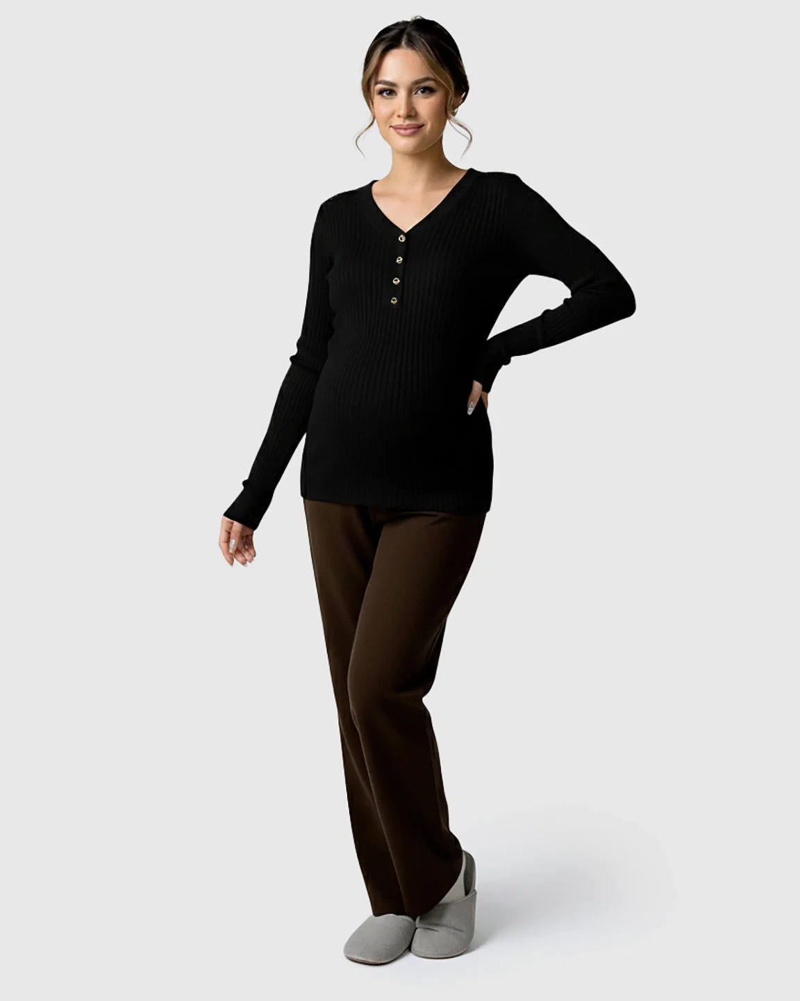 Woman wearing a black ribbed V-neck maternity nursing sweater with gold buttons and brown pants.