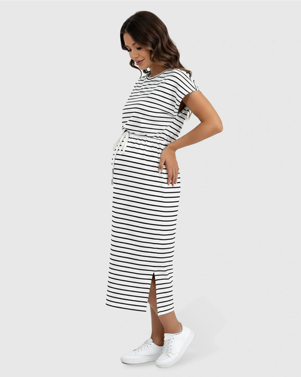Woman in a black and white striped maternity midi dress with cap sleeves, adjustable waist, and side slits.