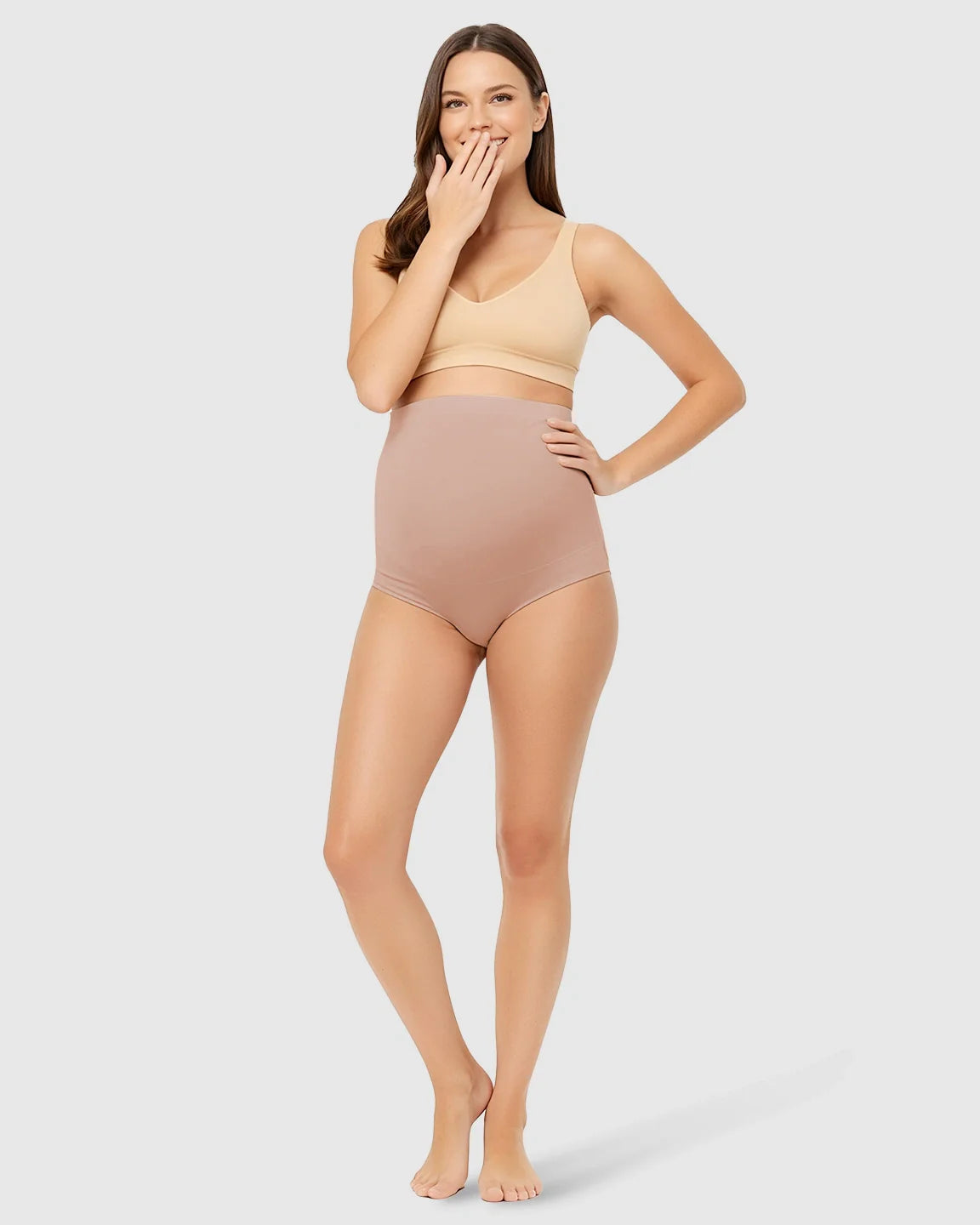 Smiling woman models high-waist seamless maternity underwear in nude, offering gentle belly support.