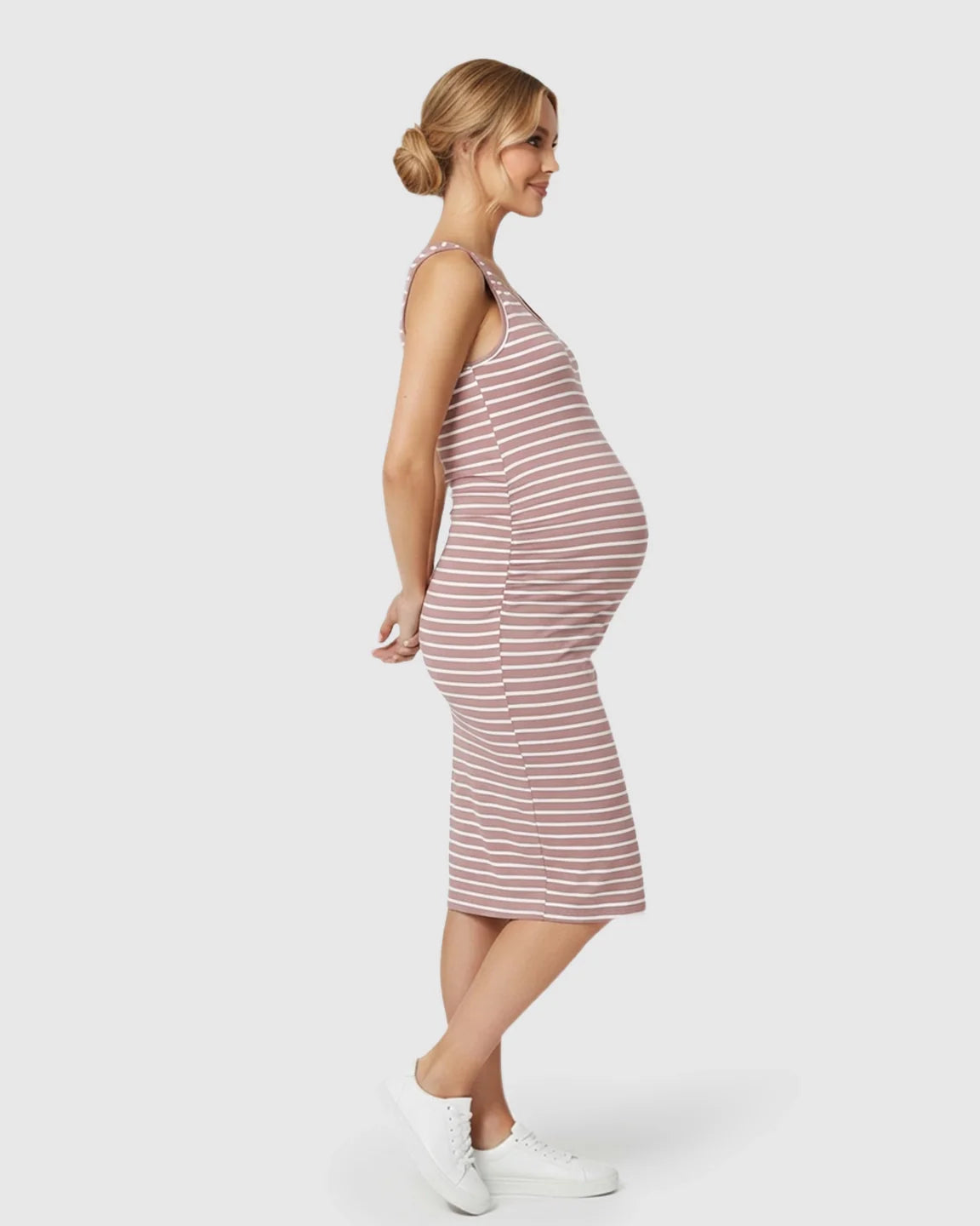 Smiling pregnant woman in a pink and white striped sleeveless bodycon maternity dress with side pleats.