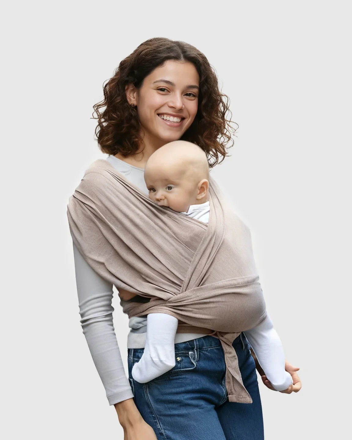 Smiling woman wearing a soft, beige adjustable wrap-around baby carrier with a baby snuggled inside.