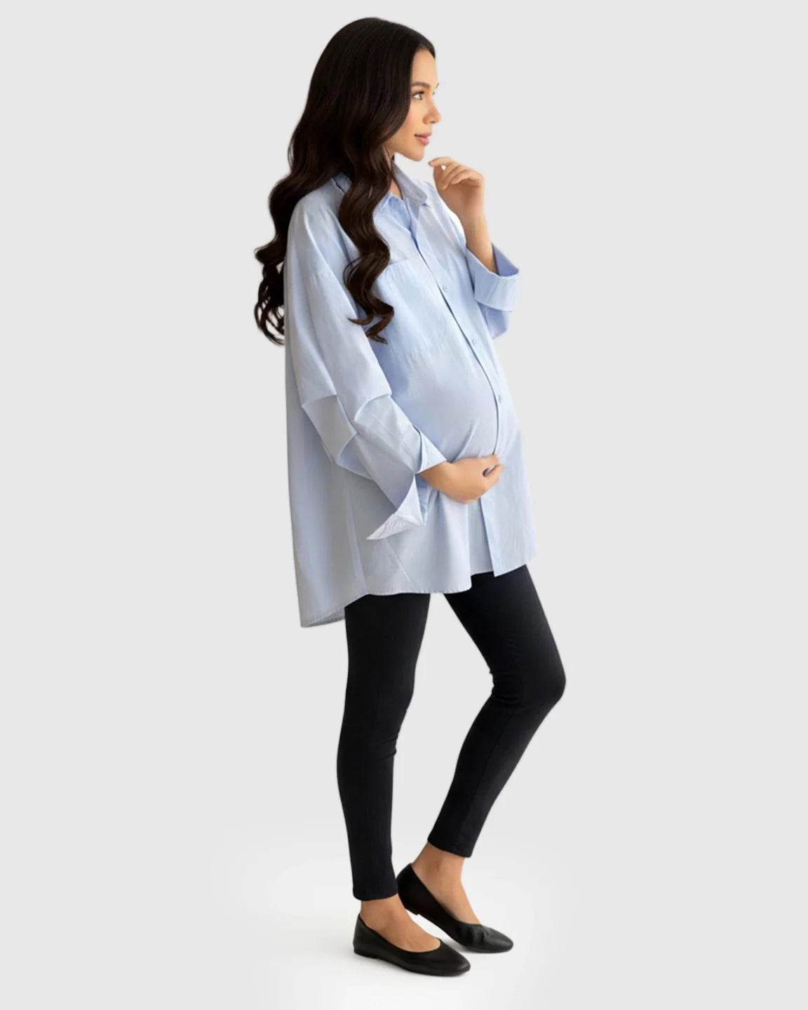 Pregnant woman in a light blue cotton lapel-collar button-front maternity tunic and black leggings.