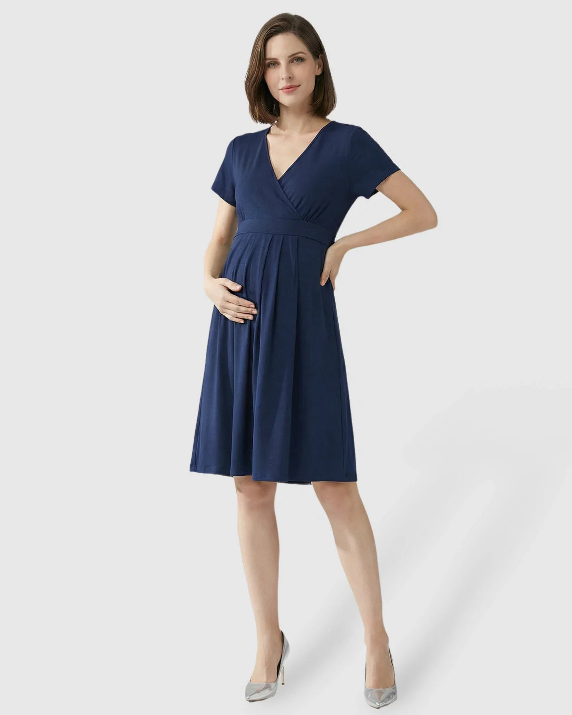 Woman in a navy V-neck A-line maternity and nursing dress with short sleeves, holding her pregnant belly.