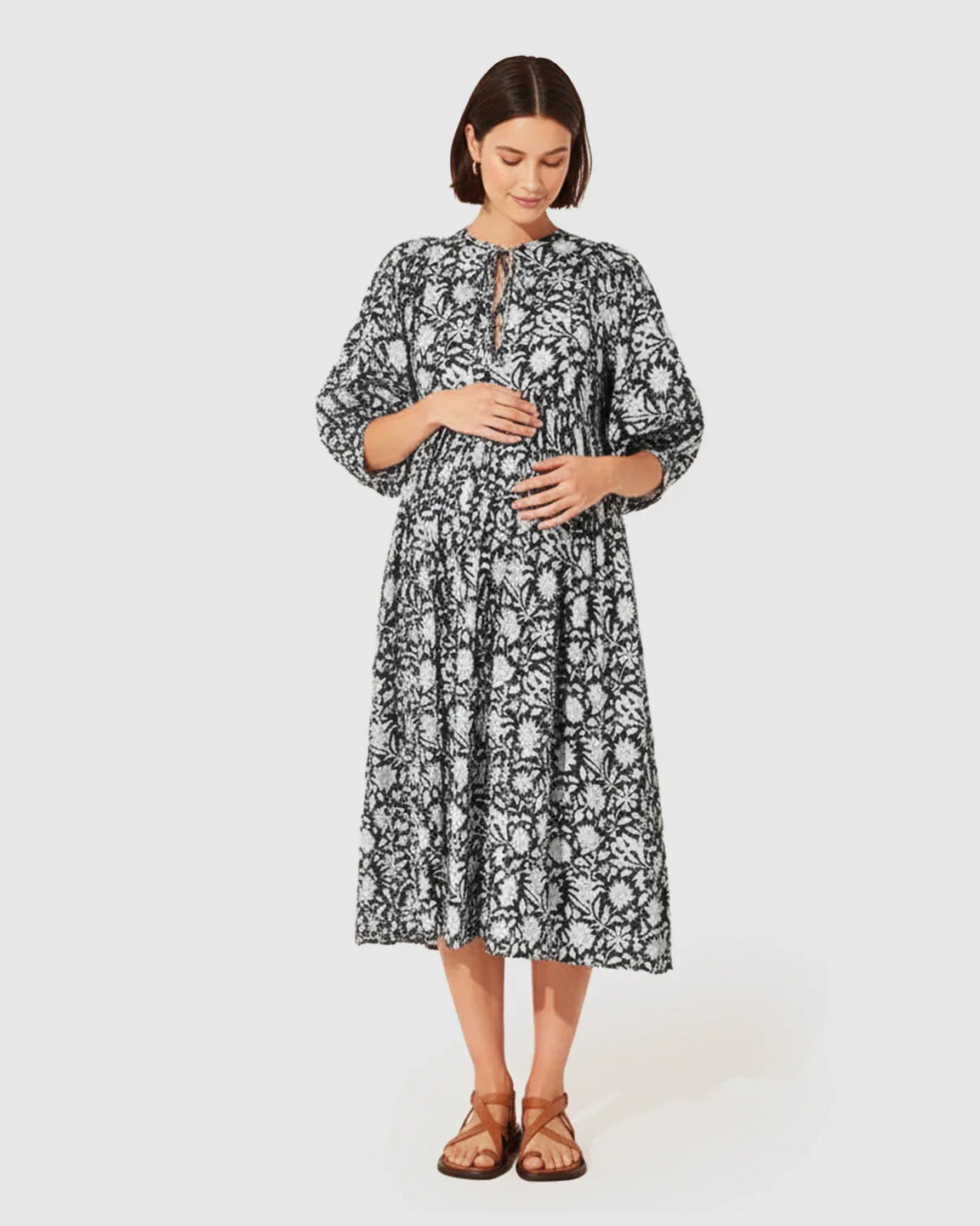 Woman in a black and white floral maternity midi dress with gathered shoulders and puff sleeves.