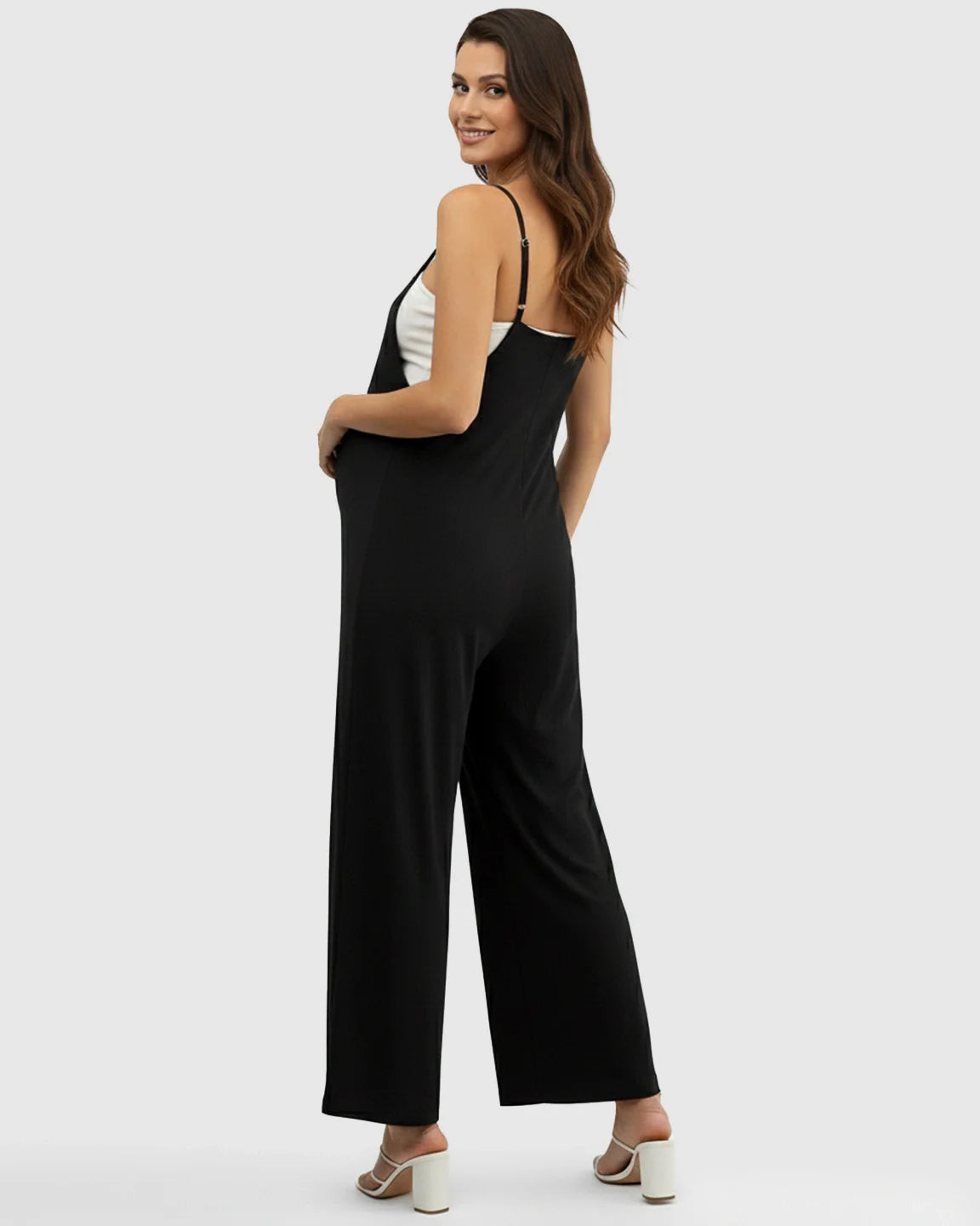 Smiling pregnant woman in a black spaghetti strap wide-leg maternity jumpsuit with a white top underneath.