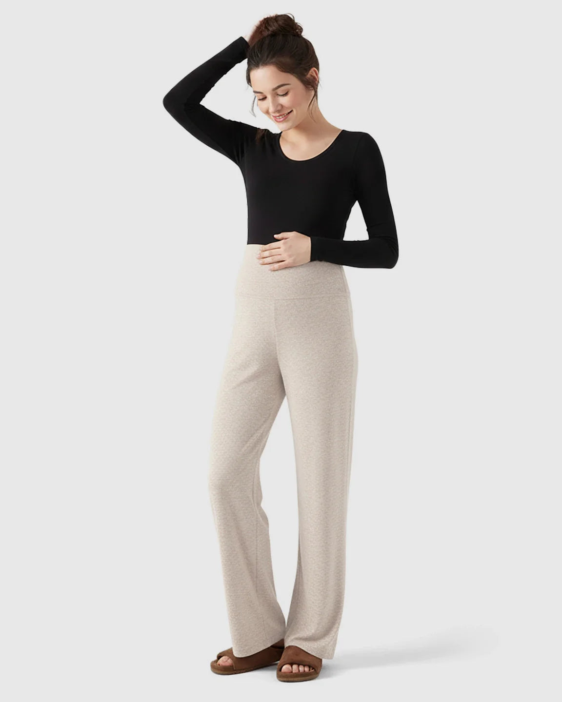 Smiling pregnant woman in beige fleece wide-leg maternity pants with over-belly waistband and black long-sleeve top.