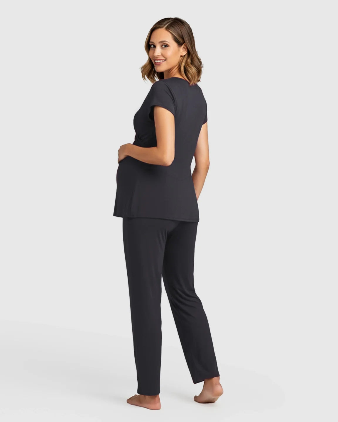 Smiling pregnant woman models a black short-sleeve maternity & nursing sleepwear set with a wrap top and loose pants.