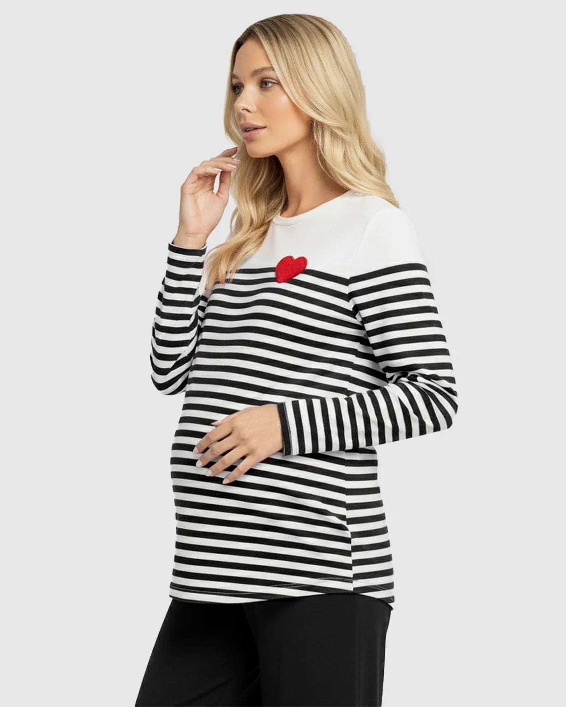 Blonde pregnant woman wearing a black and white striped long-sleeve maternity top with a red heart detail.