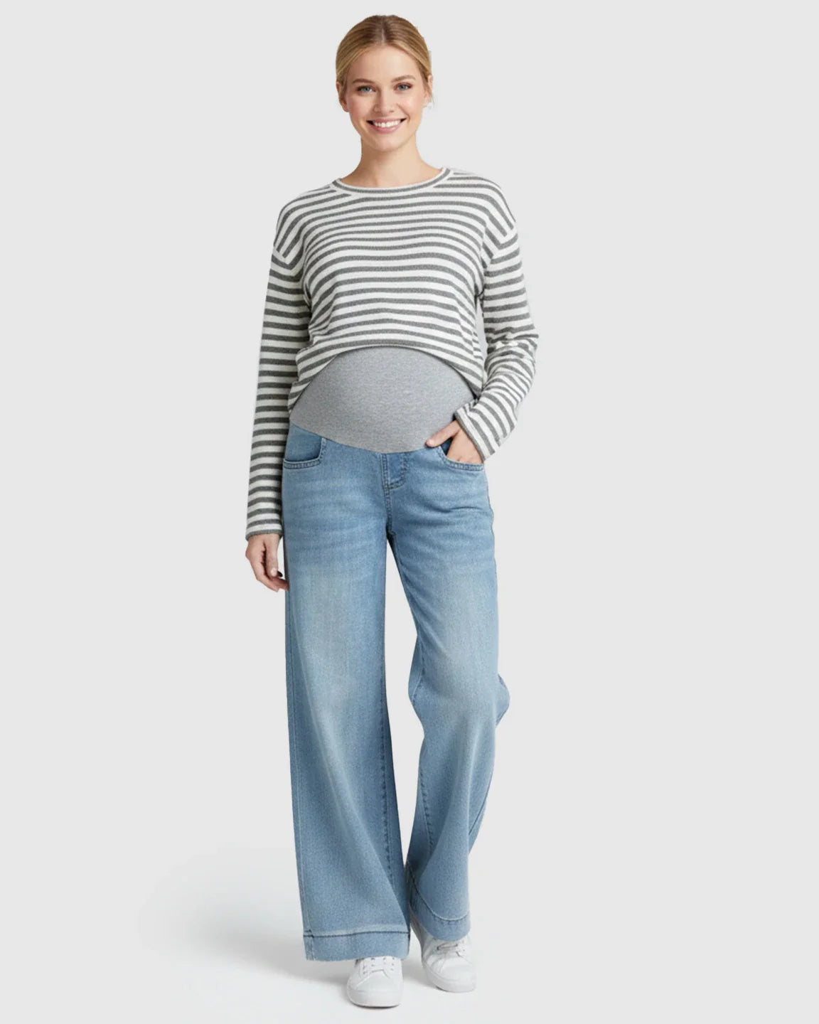 Smiling pregnant woman wearing light blue wide-leg maternity jeans with a folded hem and a grey belly band.