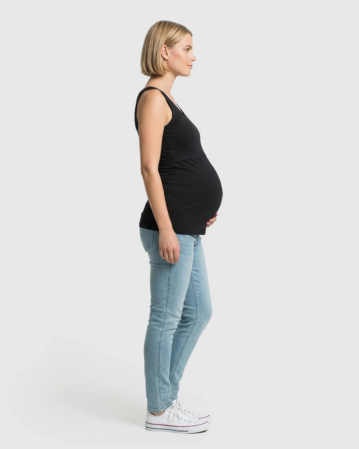 Pregnant woman in black stretch nursing-access maternity tank top and light blue jeans.