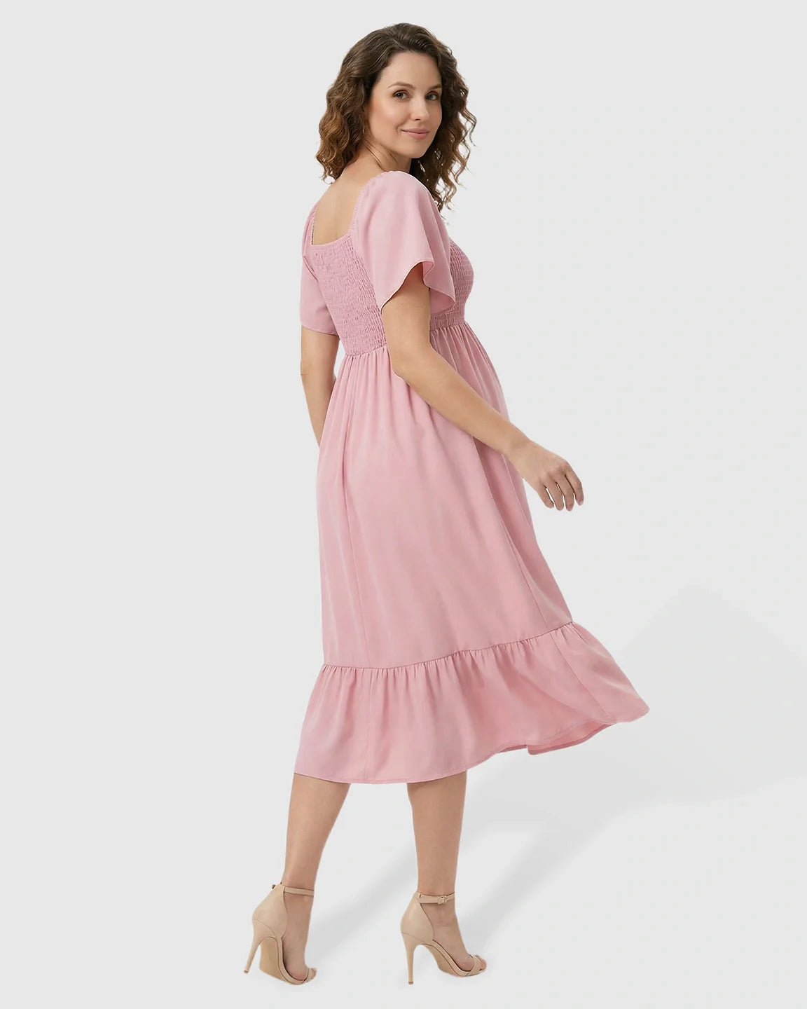 Pink flutter-sleeve smocked maternity midi dress with tiered skirt, worn by a smiling pregnant woman.