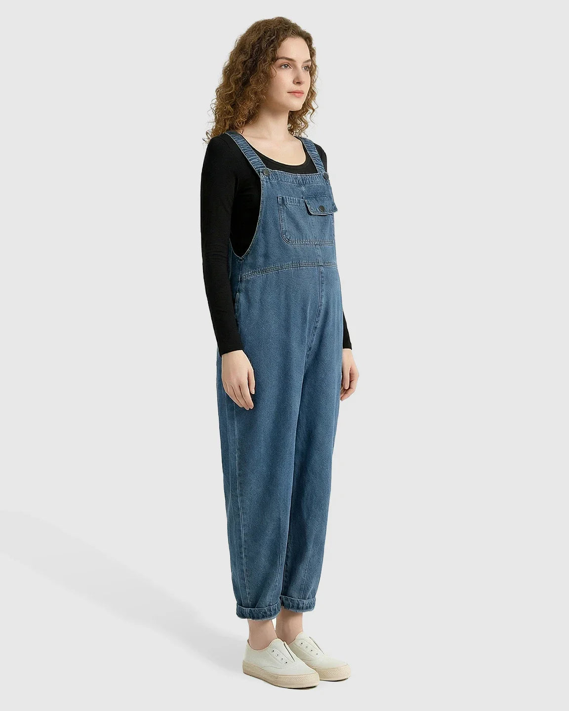 Loose-fit blue denim maternity overalls with adjustable straps and front pocket, worn over a black long-sleeve shirt.