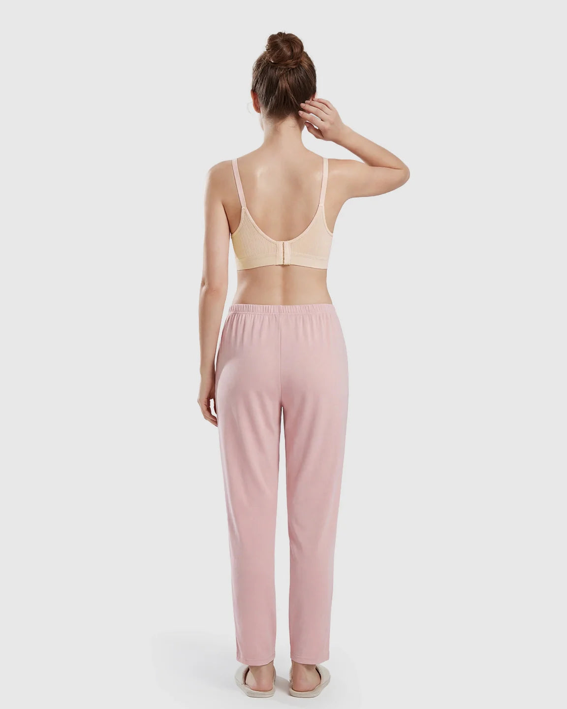 Woman from behind wearing a seamless, wireless, light peach nursing bra with textured cups and pink lounge pants.