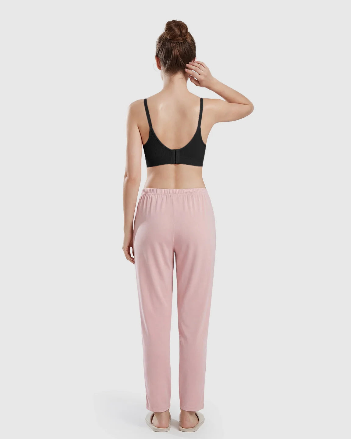 Model from behind wearing a black seamless cross-front wireless nursing bra with pink lounge pants.