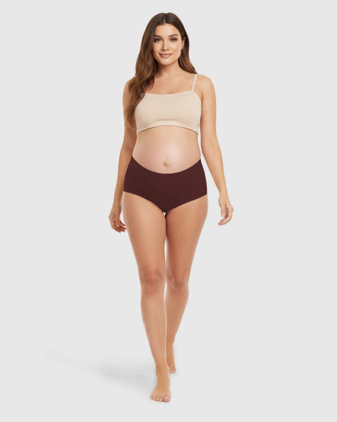 Smiling pregnant woman in seamless high-waist maroon maternity underwear and a beige crop top.