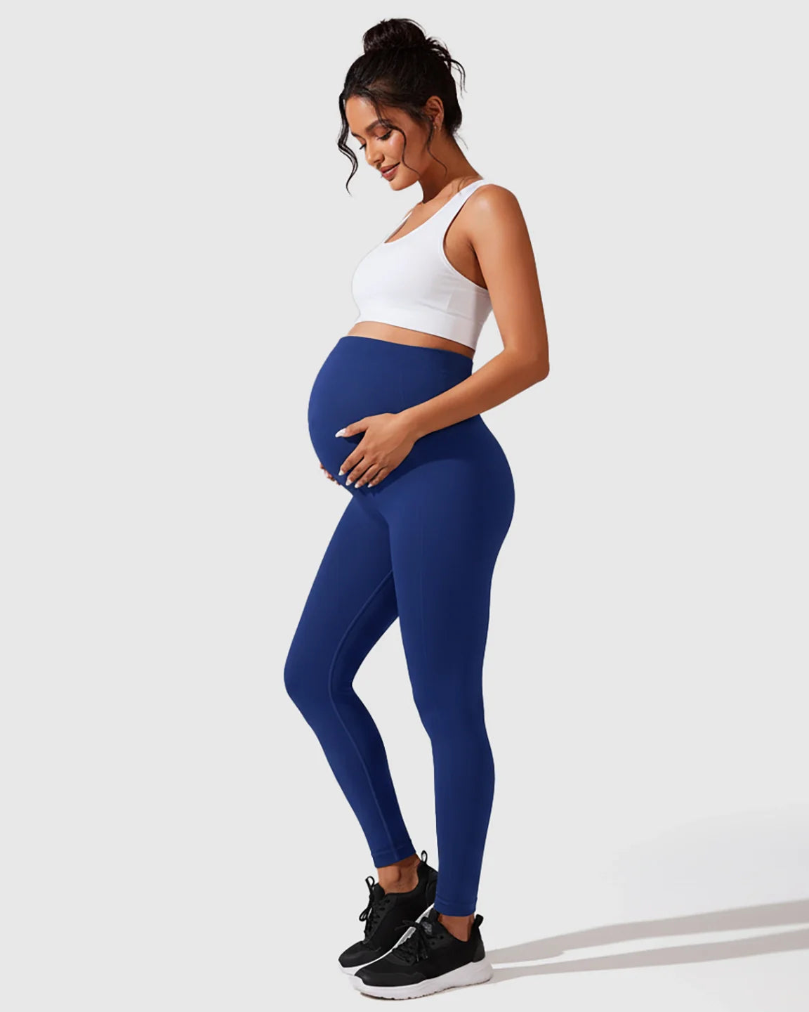 Pregnant woman in royal blue seamless maternity leggings with full-belly support, paired with a white sports bra.