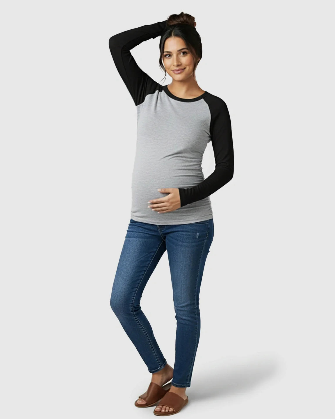 Smiling pregnant woman in a gray and black raglan sleeve maternity top with side ruching and blue jeans.
