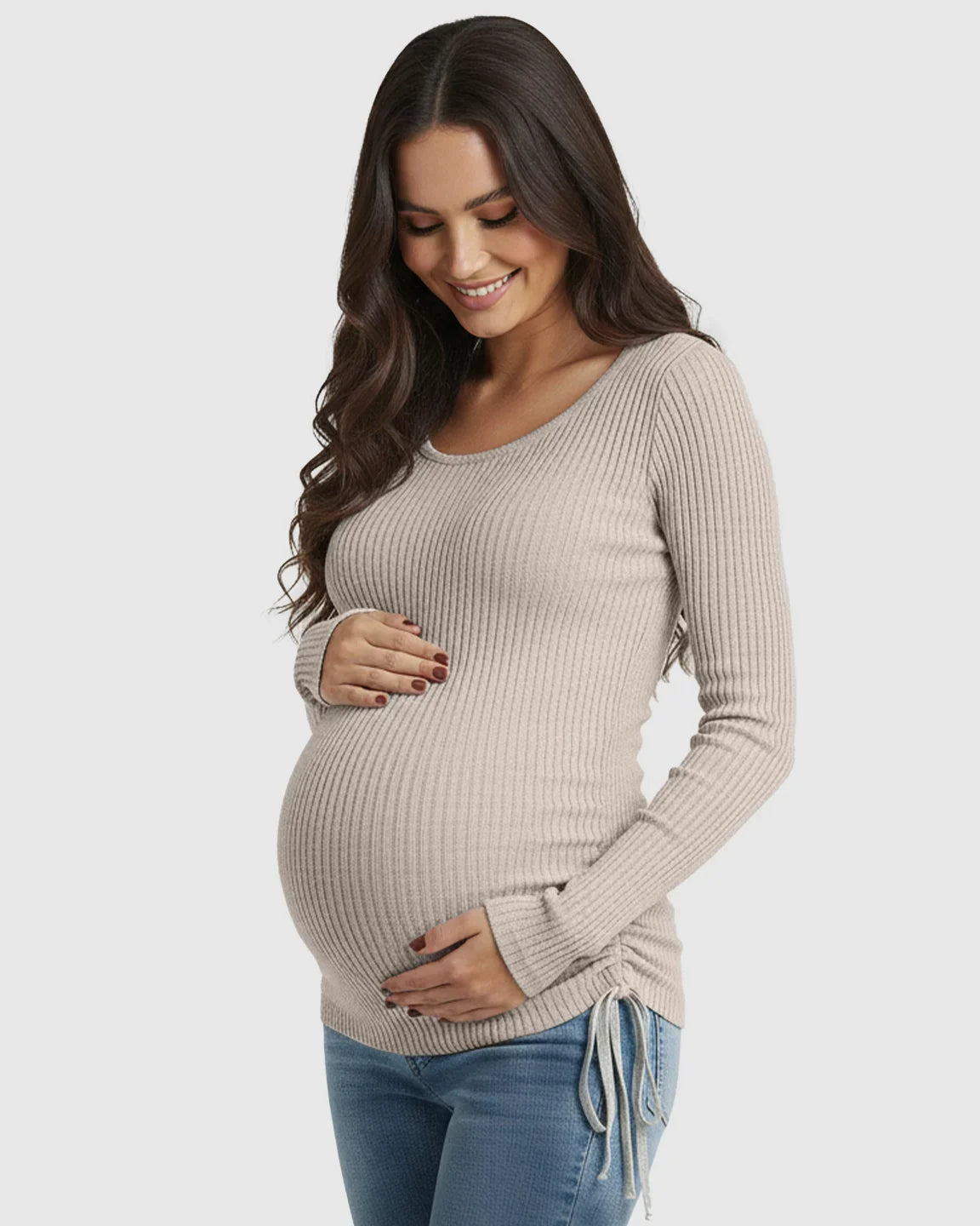 Smiling pregnant woman in a beige ribbed long-sleeve maternity top with adjustable side drawstrings.