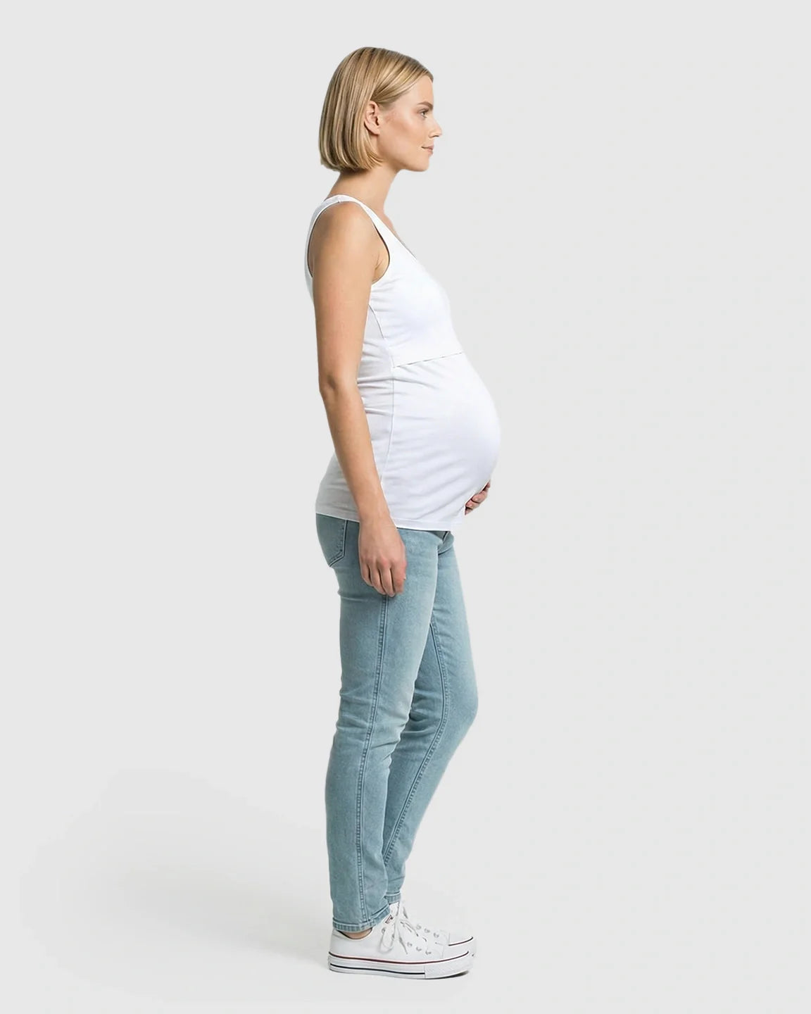 Pregnant model in a white stretch nursing-access maternity tank top and light wash jeans.