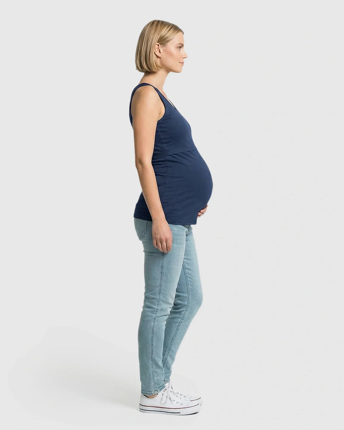 Pregnant woman in a navy stretch nursing-access maternity tank top and light wash jeans.