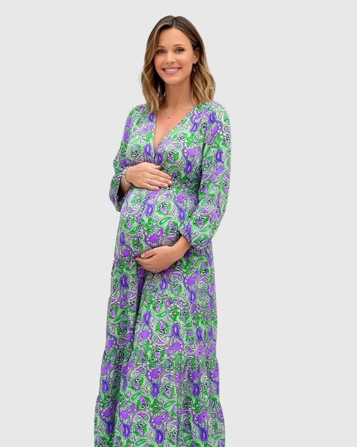 Pregnant woman in a green and purple paisley flowy maxi dress with a V-neck and tie waist.
