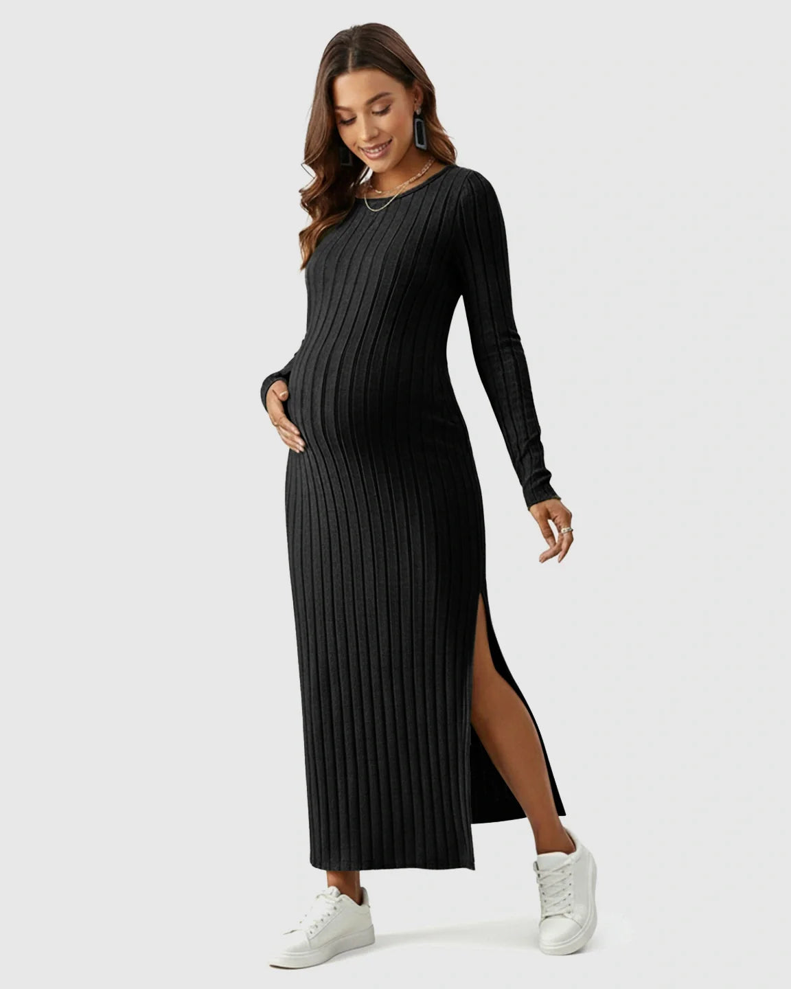 Pregnant woman in a black ribbed knit long-sleeve maxi dress with a side slit, wearing white sneakers.