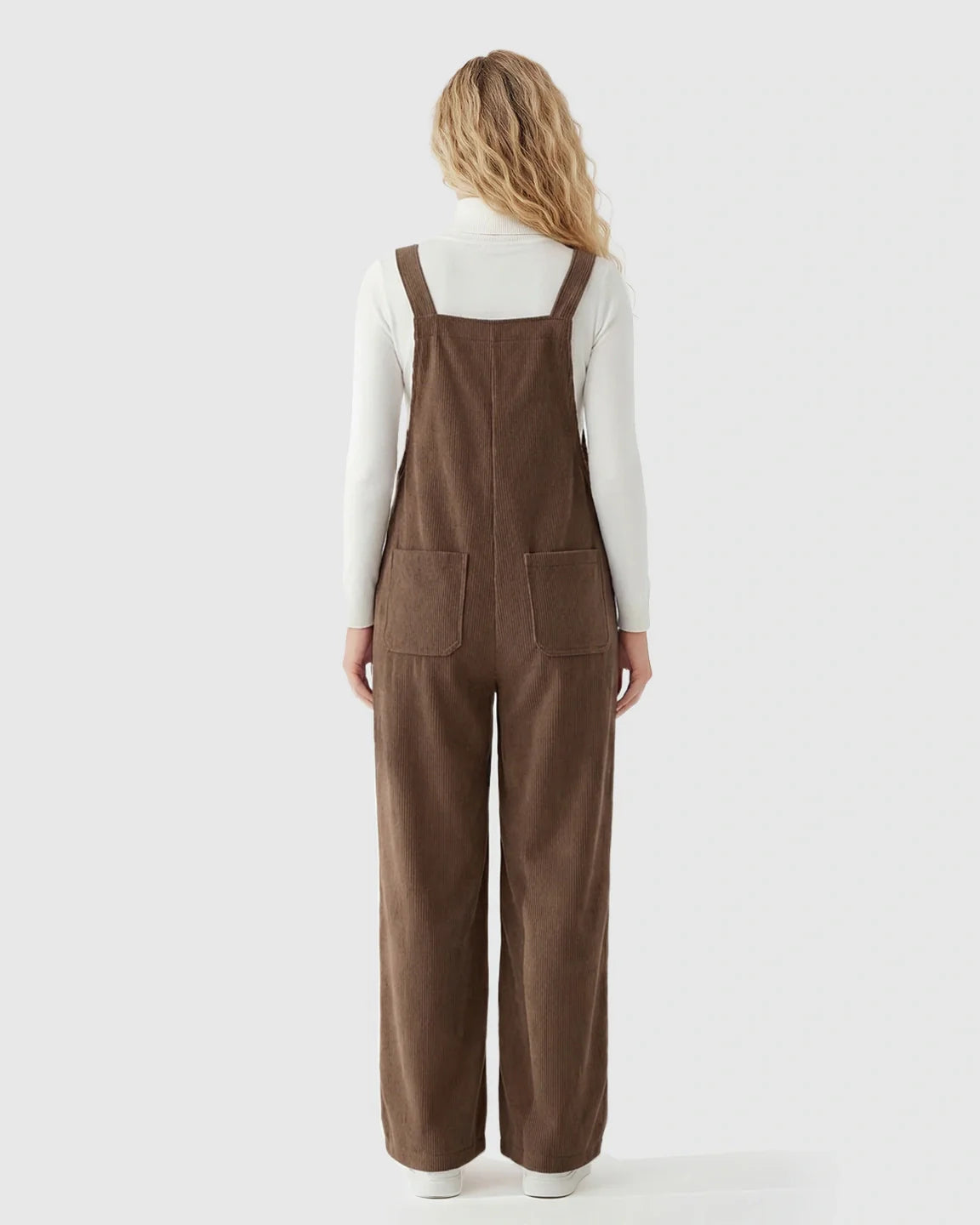 Woman from behind wearing brown corduroy maternity overalls with adjustable straps over a white turtleneck.