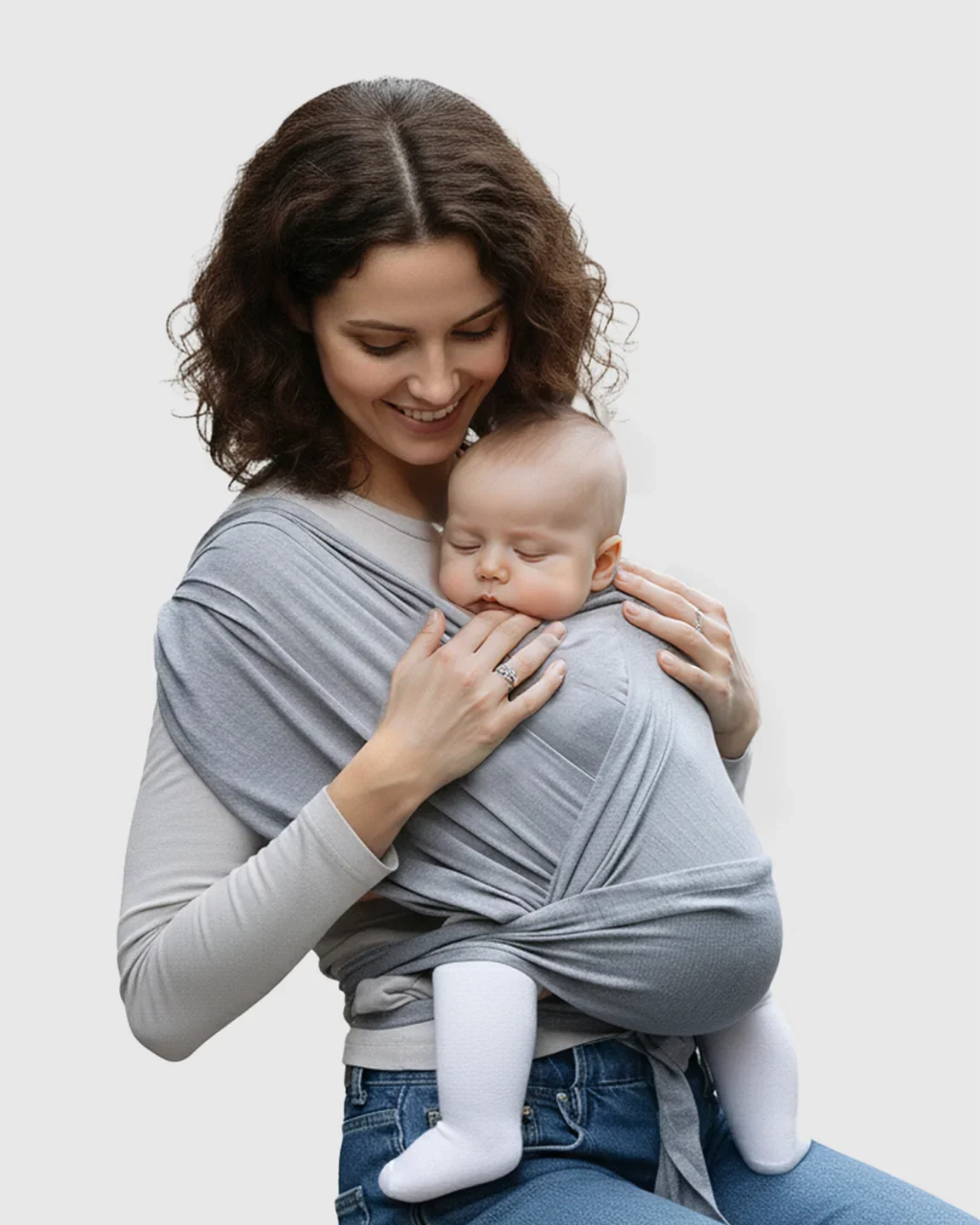 Smiling mom cradles sleeping baby in a soft gray adjustable wrap-around baby carrier.