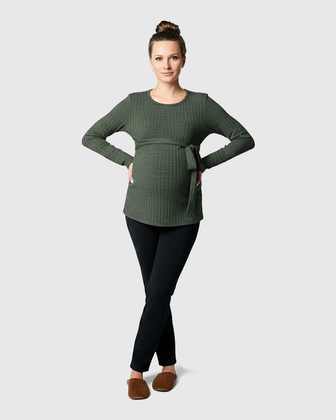 Woman in a ribbed olive green maternity sweater with a tie-waist, black pants, and brown slippers.