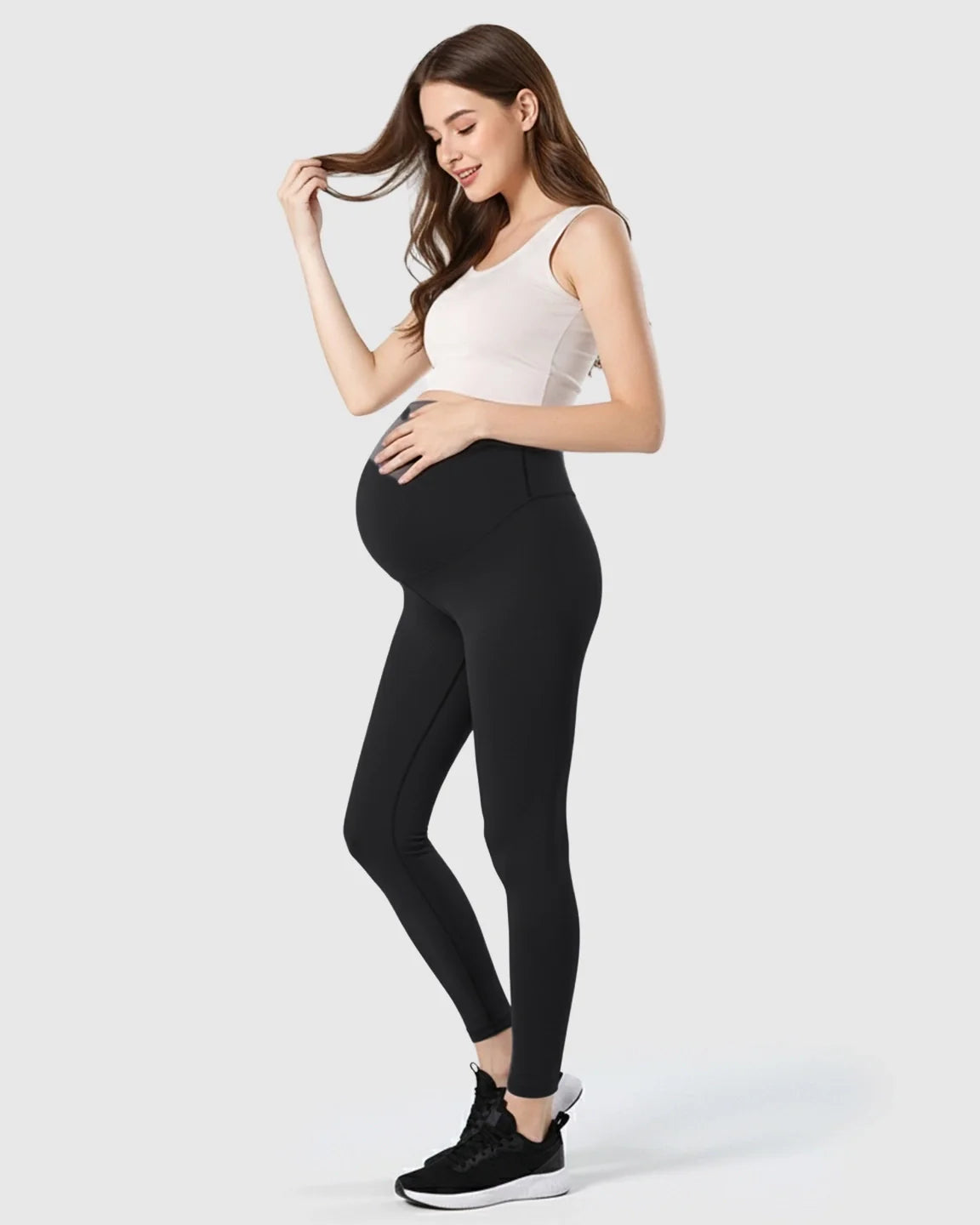Smiling pregnant woman in black double-layer belly support maternity leggings and a white tank top.