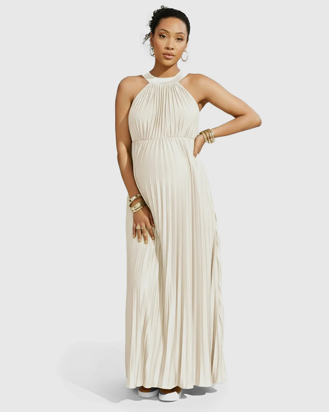 Pregnant model in a cream faux silk halter neck pleated maxi dress with gold bracelets.