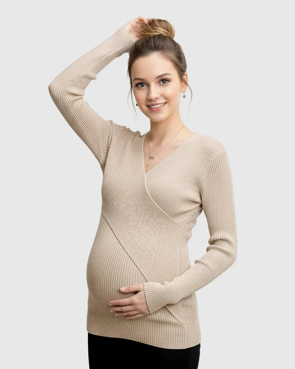 Smiling pregnant woman in a beige ribbed faux-wrap maternity top, holding her bump.