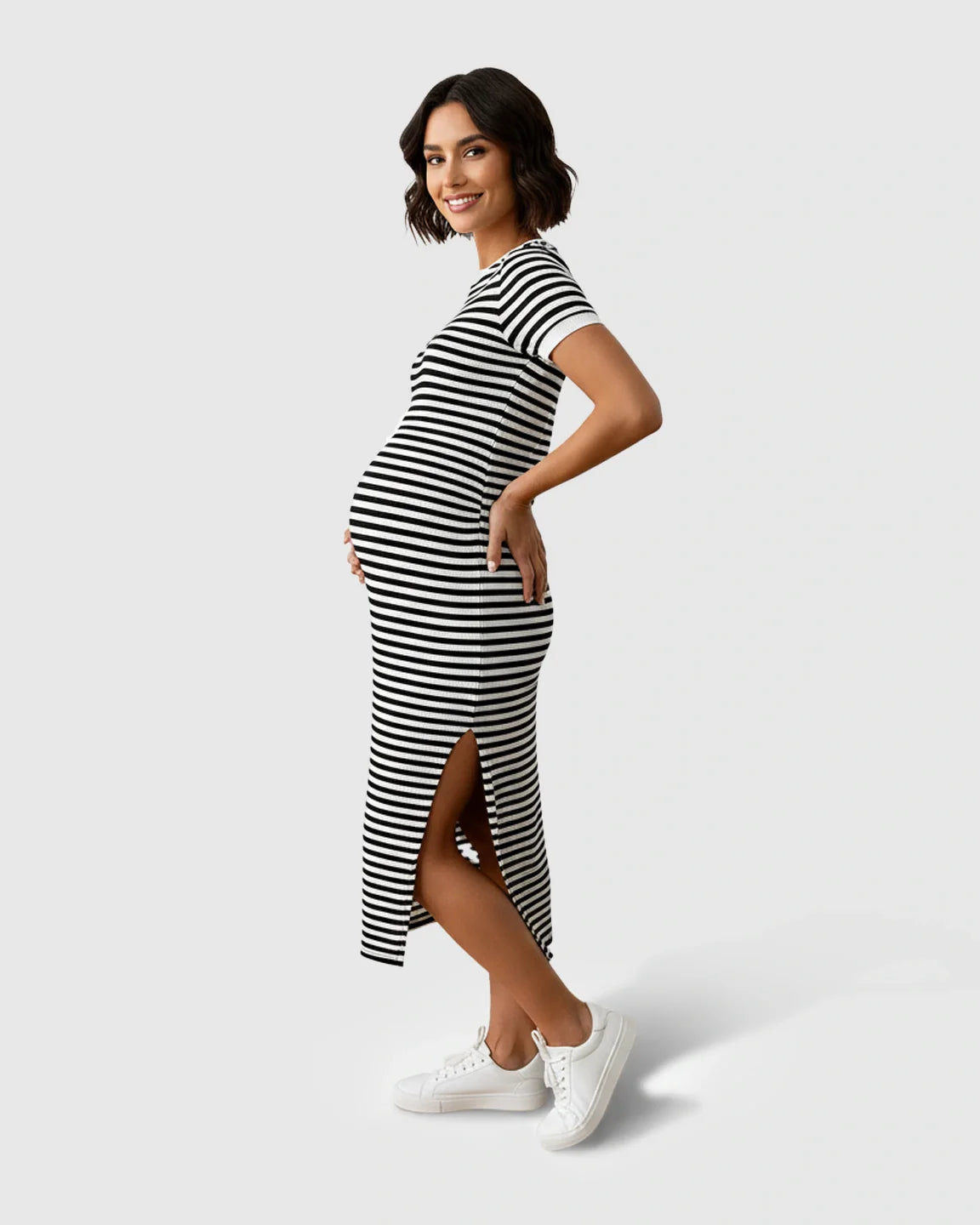 Smiling pregnant woman in a black and white striped side-slit maternity column dress and white sneakers.