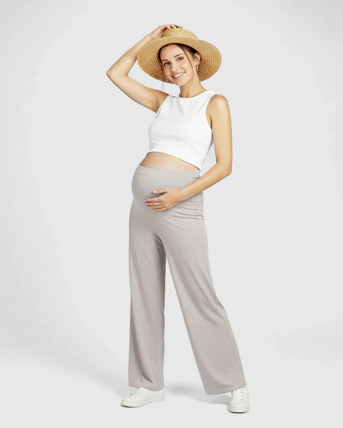 Smiling pregnant woman in a white crop top, straw hat, and gray Comfort Fit elastic waist maternity pants.
