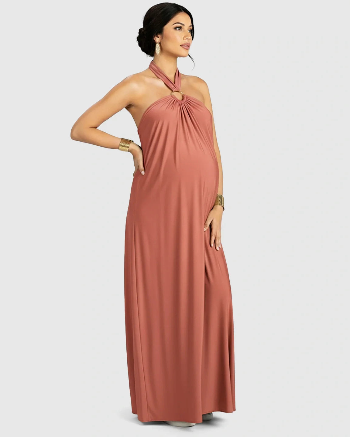 Maternity model in a terracotta backless halter neck maxi dress with a gold ring detail.